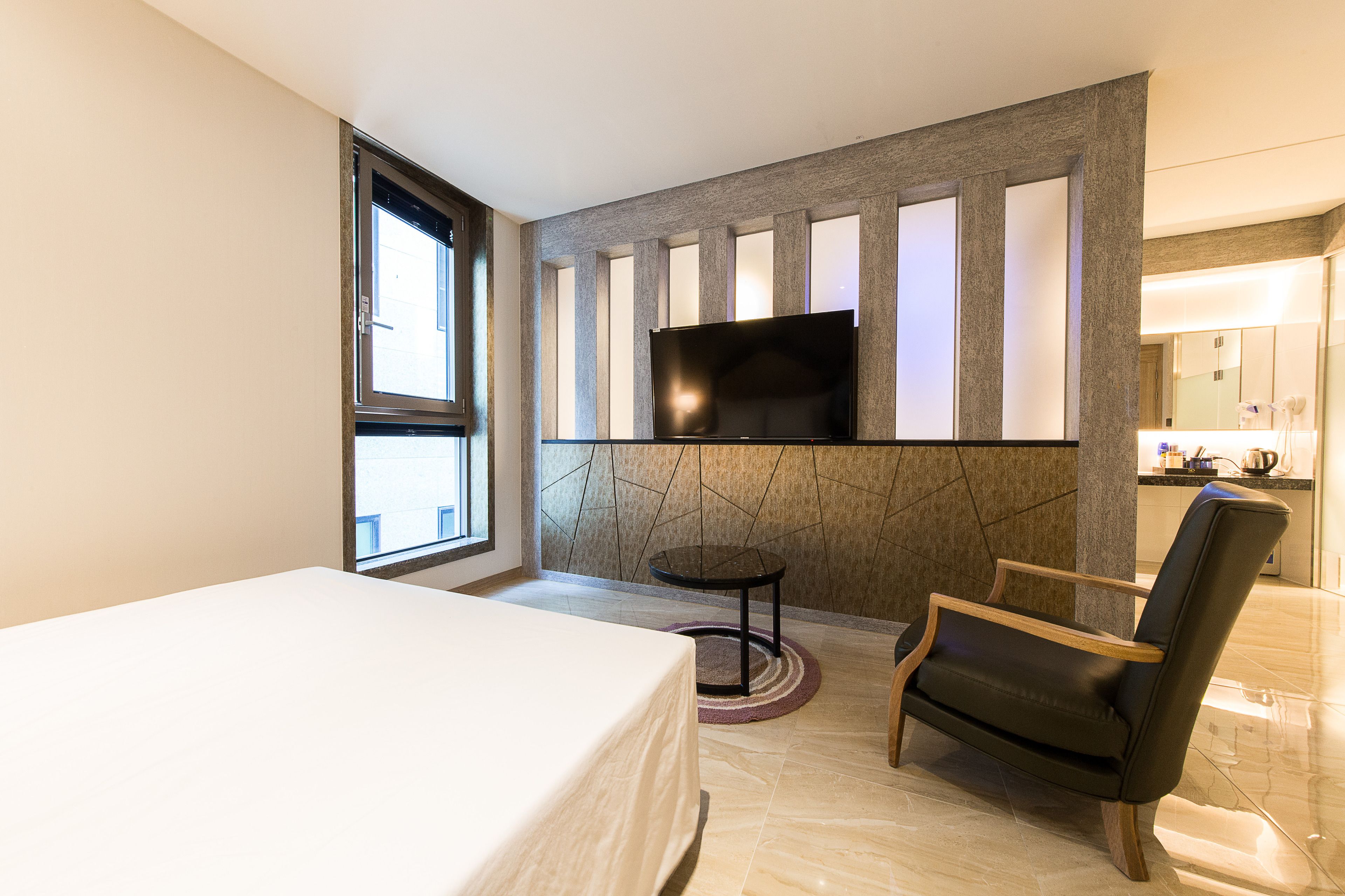 A modern hotel room with a bed, a TV mounted on a wall, a chair, and a small table.