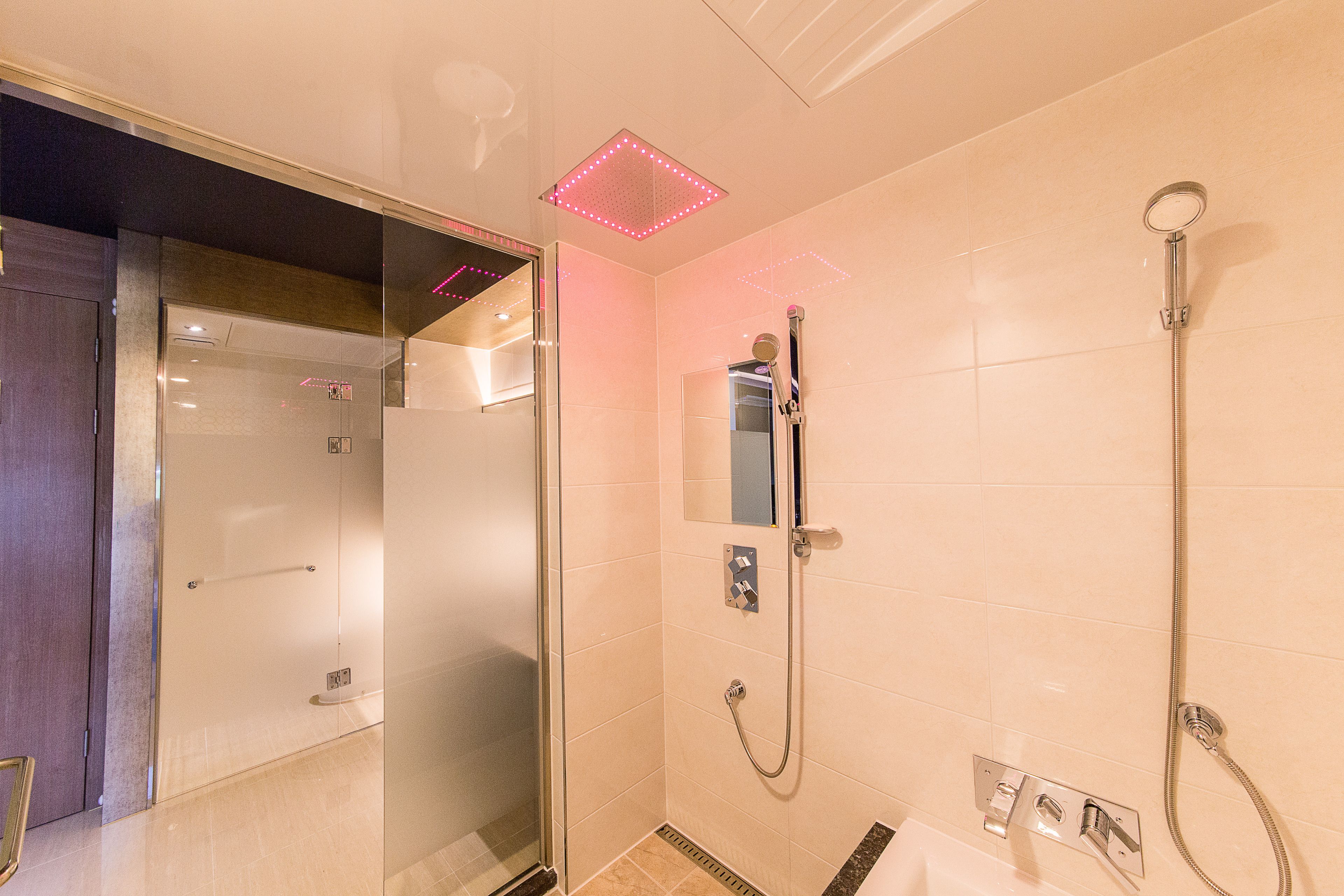 A modern bathroom with a glass shower enclosure, a handheld showerhead, and a wall-mounted control panel.