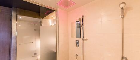 A modern bathroom with a glass shower enclosure, a handheld showerhead, and a wall-mounted control panel.