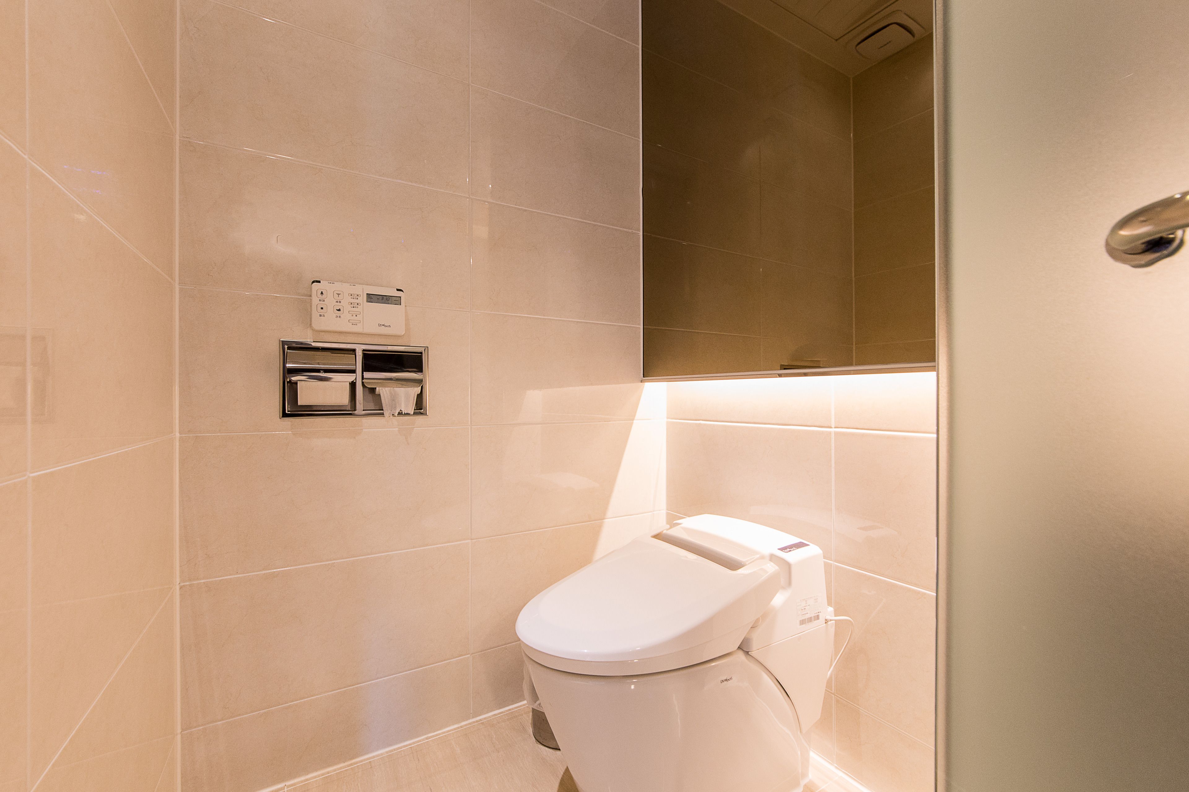 A modern bathroom with a toilet, a hand dryer, and a paper towel dispenser.