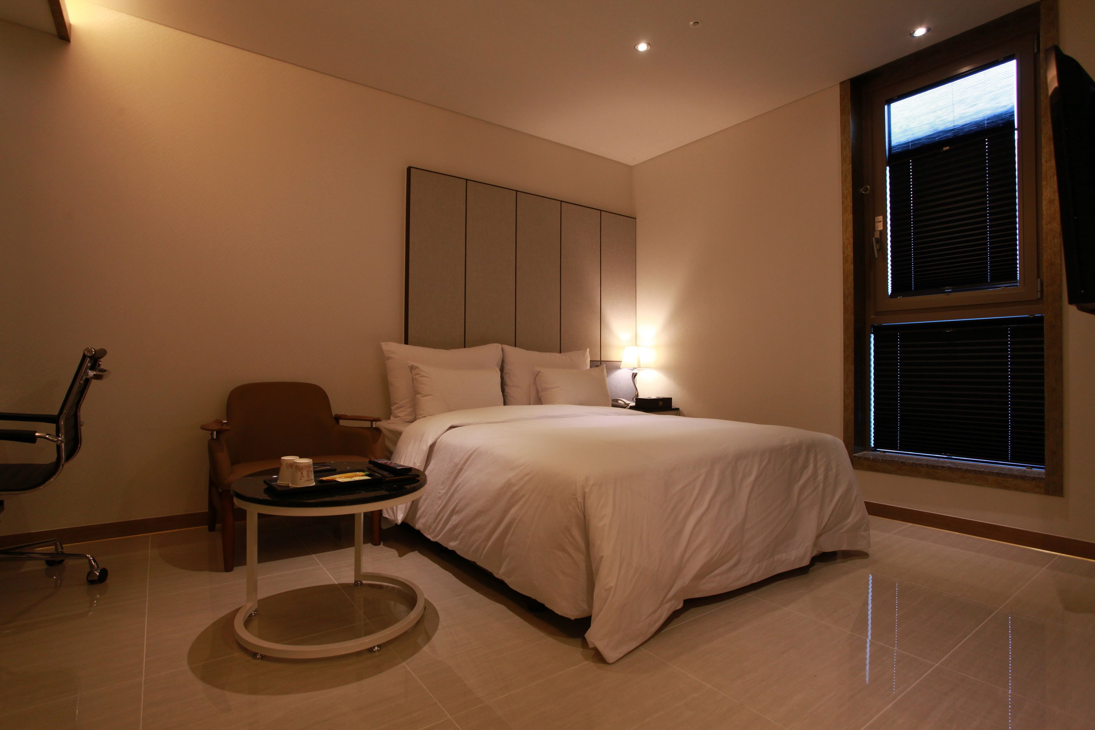 A hotel room with a bed, a small round table, a chair, and a window with blinds.