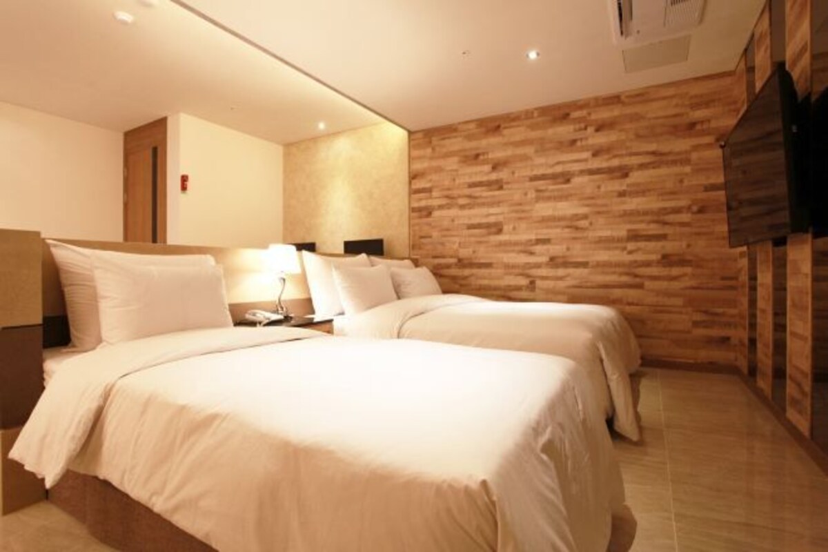 Quarto de hotel com duas camas, um painel de parede em madeira e uma televisão de tela plana fixada na parede.