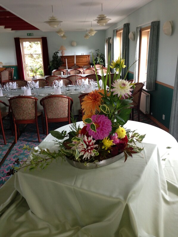 A dining area with round tables set for a meal, chairs, and a floral centerpiece. - Hotel E4 (Rodby)