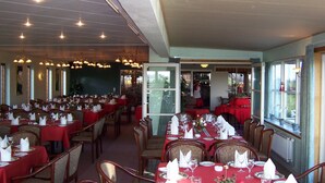 Un vaste espace dédié à la salle à manger, avec plusieurs tables dressées, recouvertes de nappes rouges et dotées de chaises disposées avec soin.