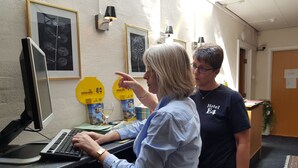 Une femme est assise à un bureau, devant un ordinateur, dans une pièce dont les murs sont ornés d’œuvres d’art encadrées, et on aperçoit un comptoir d’accueil à l’arrière-plan.