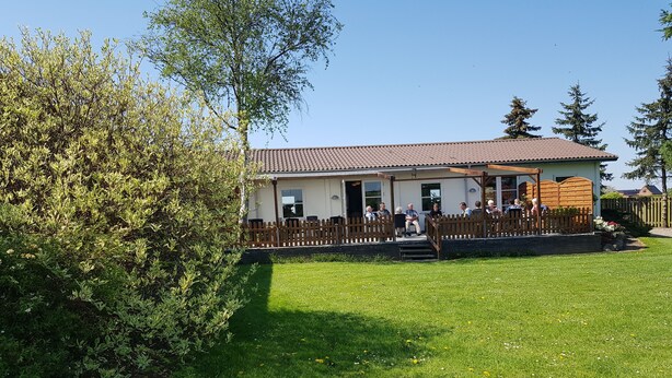 Un bâtiment avec un toit recouvert de tuiles, une clôture en bois et une pelouse verdoyante parsemée de fleurs.