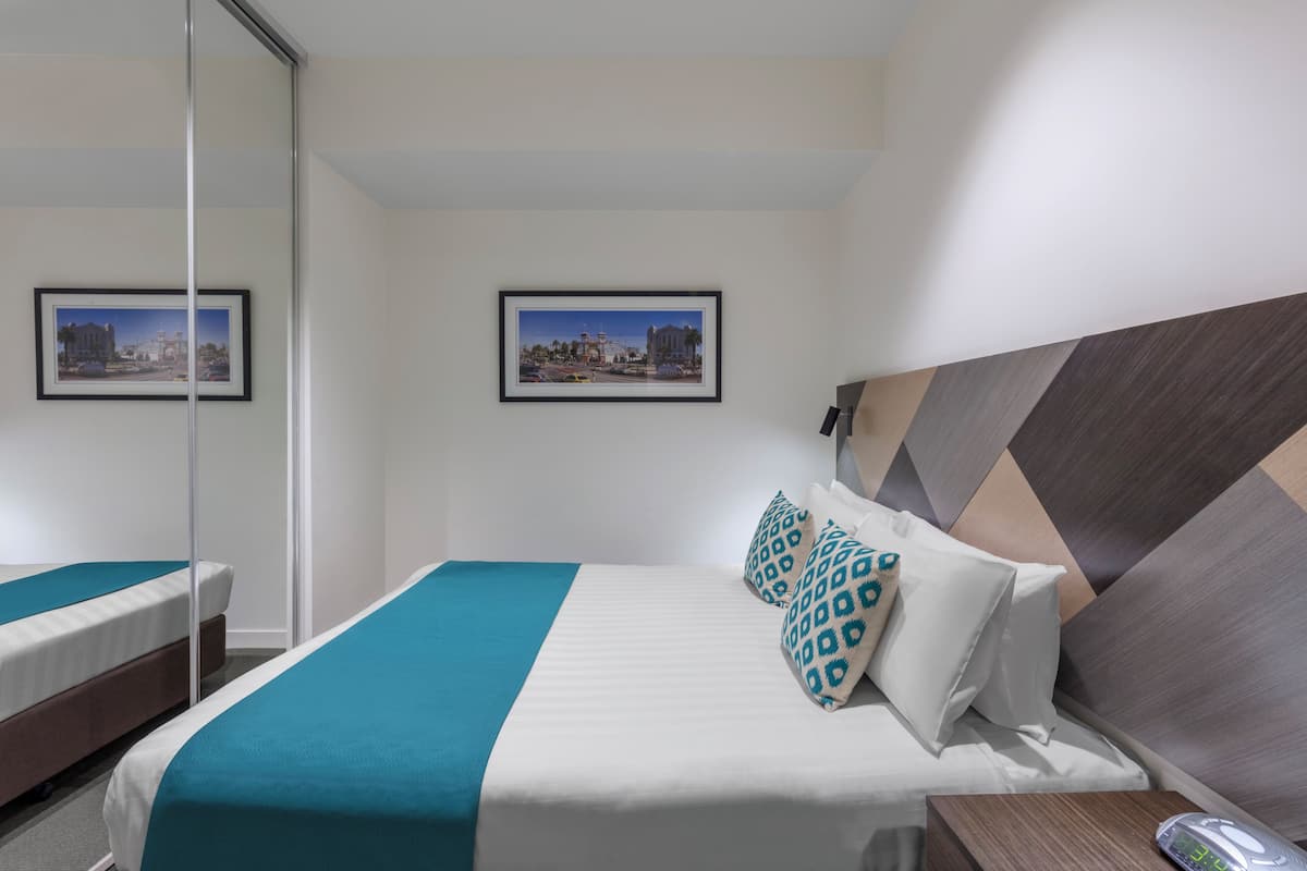 A hotel room with a bed, a bedside table, and two framed pictures on the wall.