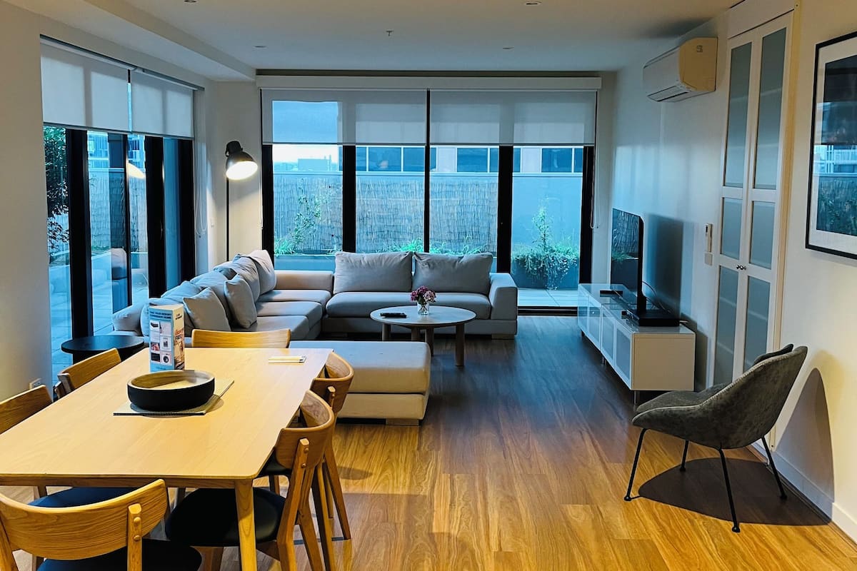 A modern living room with a dining area, large windows, and a flat-screen TV.
