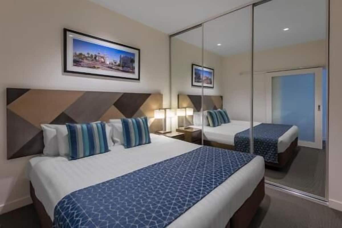 Habitación de hotel con dos camas, un espejo grande y un cuadro en la pared.