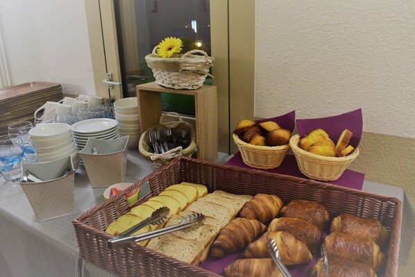 A breakfast buffet with bread, pastries, and a basket of fruits.
