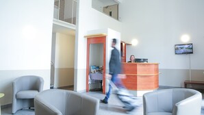 A reception area with a desk, chairs, and a TV screen. - Hôtel Inn Design Châteaubriant (Chateaubriant)