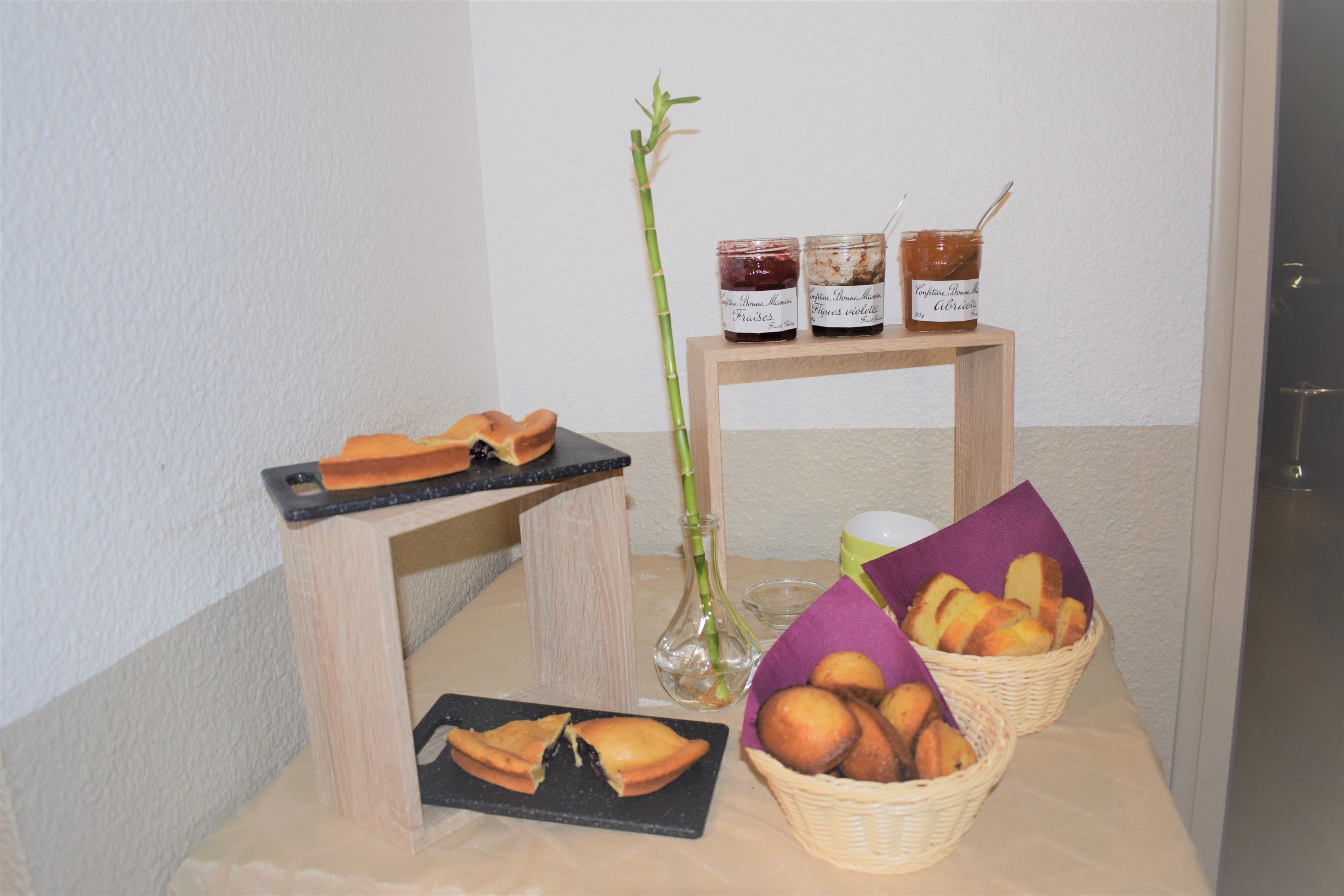 Une table avec des pâtisseries, des pots de confiture et un vase rempli de bambous.