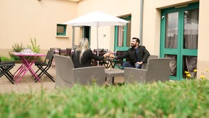 An outdoor seating area with wicker furniture and a table with a white umbrella. - Hôtel Inn Design Châteaubriant (Chateaubriant)