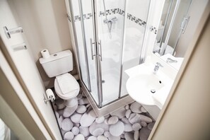 Un baño con ducha envuelta en vidrio, inodoro y lavamanos.