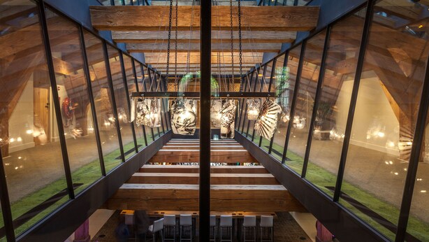 Un interior moderno con una escalera central, paredes de vidrio y vigas de madera.
