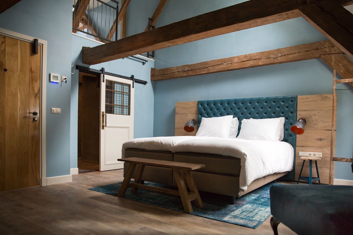 A bedroom with a wooden ceiling, a bed with white bedding, a bench, and a small stool.