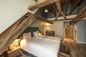 A bedroom with a loft-style ceiling, a bed with white linens, a nightstand with a lamp, and wooden beams. - Stadshotel Woerden (Woerden)