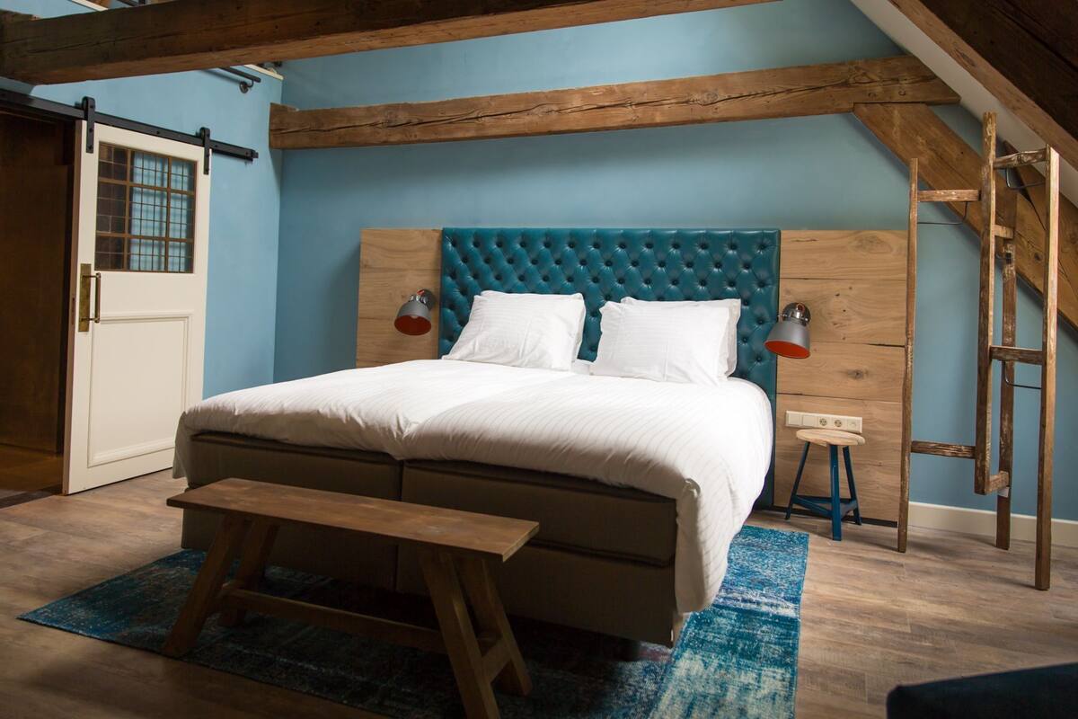 A bedroom with a large bed, wooden headboard, two bedside lamps, a bench, and a blue rug.