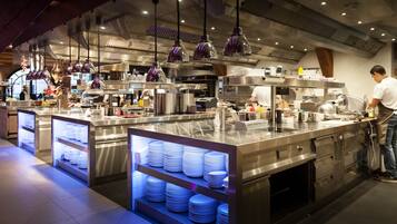 A modern kitchen with stainless steel appliances, overhead purple pendant lighting, and neatly stacked white plates on display.