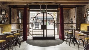 Interior de restaurante con pared de ladrillo, techo de madera y zona de estar circular con taburetes y mesas.