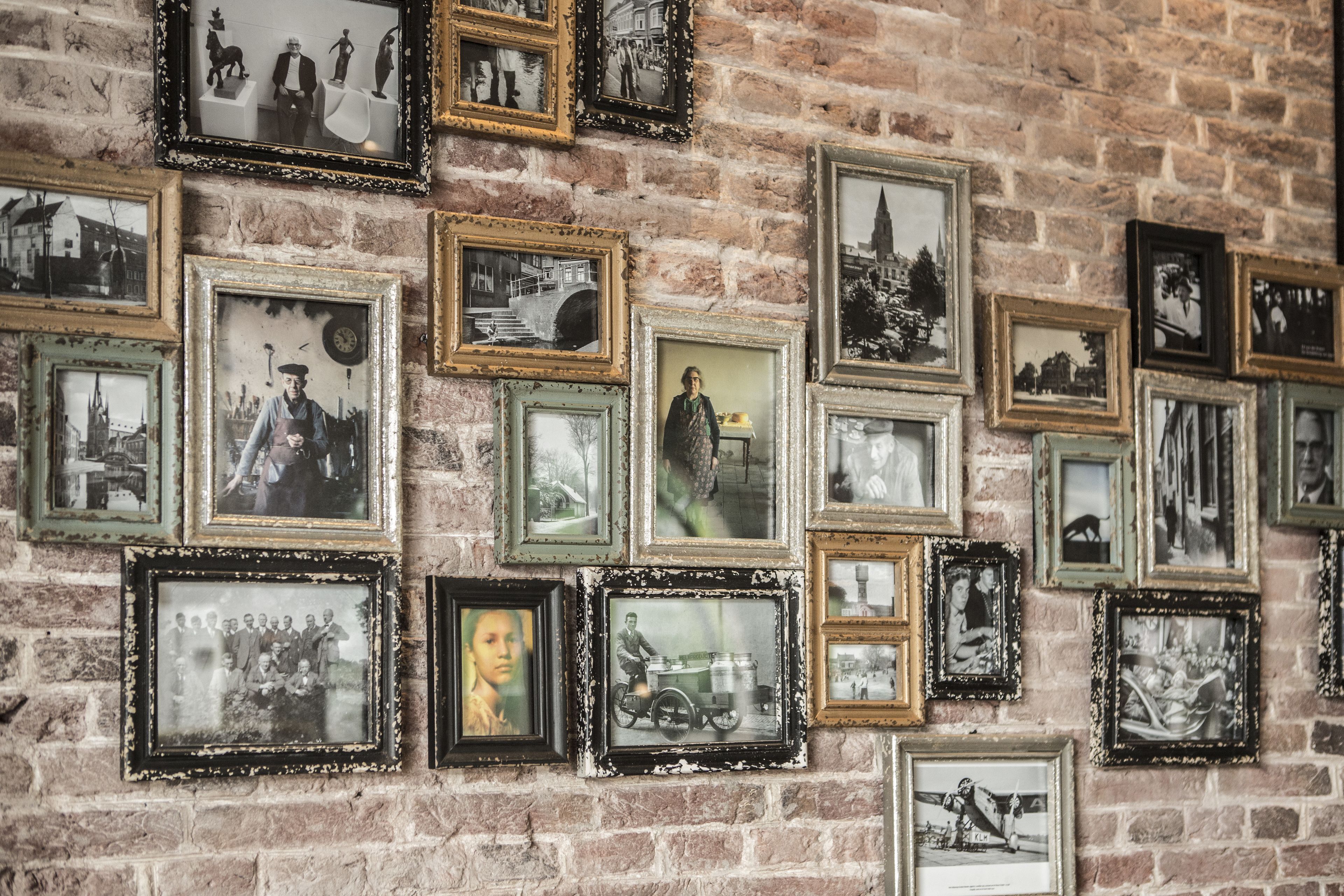 A brick wall with multiple framed photographs of various scenes and people.