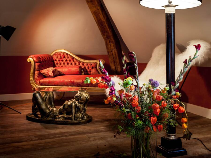 A room with a red sofa, a floor lamp, and a vase of flowers.