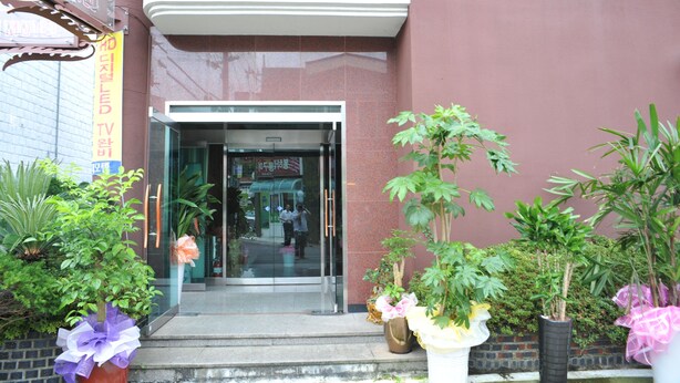 A hotel entrance with a glass door, steps leading up to it, and potted plants on either side. - Jeju Olleh Hotel (Jeju City)