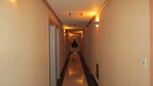 A hotel hallway with a tiled floor, doors on both sides, and wall-mounted light fixtures. - Jeju Olleh Hotel (Jeju City)