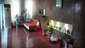 A hotel lobby with a red leather sofa, a reception desk, a wall-mounted TV, and several potted plants. - Jeju Olleh Hotel (Jeju City)