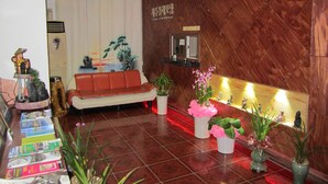 A reception area with a wooden reception desk, a red sofa, and several potted plants. - Jeju Olleh Hotel (Jeju City)