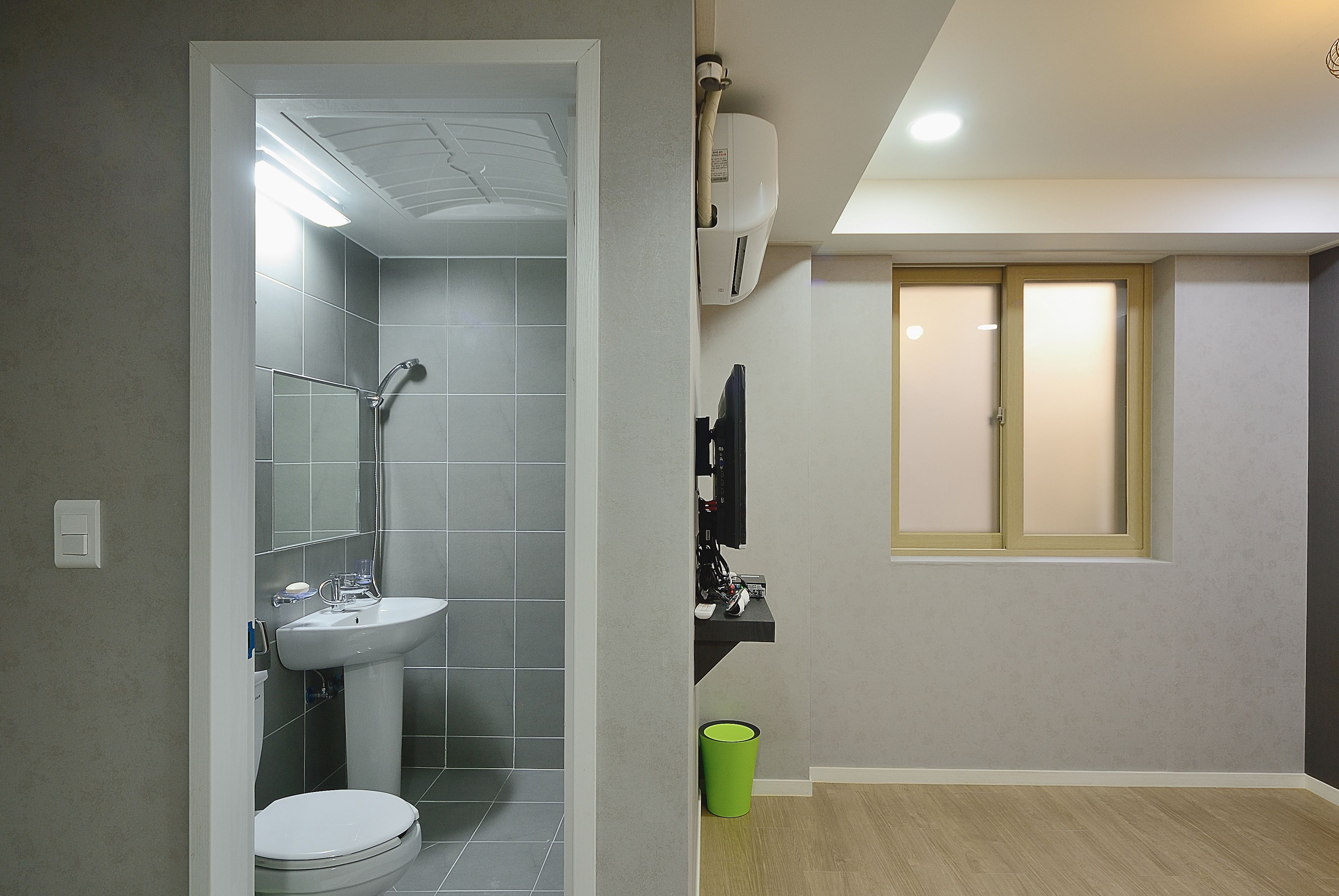 A bathroom with a toilet, sink, and shower. There is a green trash bin and a towel rack.