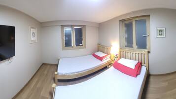 A room with a bed, a TV mounted on the wall, a window, and an air conditioning unit.