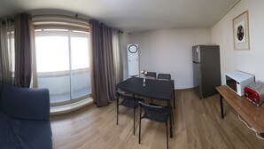 Un espacio habitable compacto con sofá, una mesa de comedor con sillas, microondas, tostadora y refrigerador.