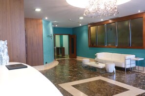 A hotel lobby with a reception desk, a white sofa, a small table, and a chandelier.