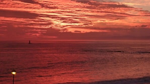 A sunset over the ocean with a lighthouse in the distance.