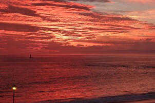 Um pôr do sol sobre o oceano, com um farol ao longe.