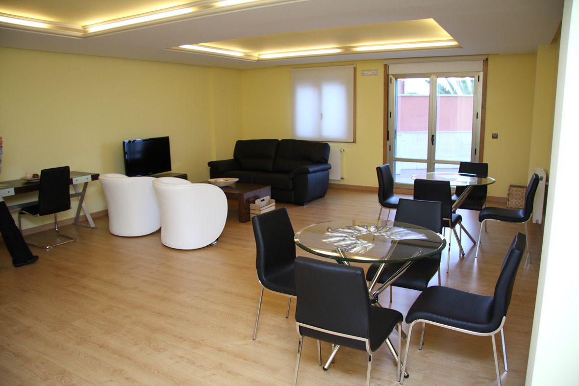 A modern room with a glass-top table, black chairs, a black sofa, a television, and a large window.