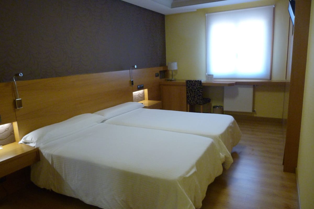 A hotel room with two beds, a desk, and a window.