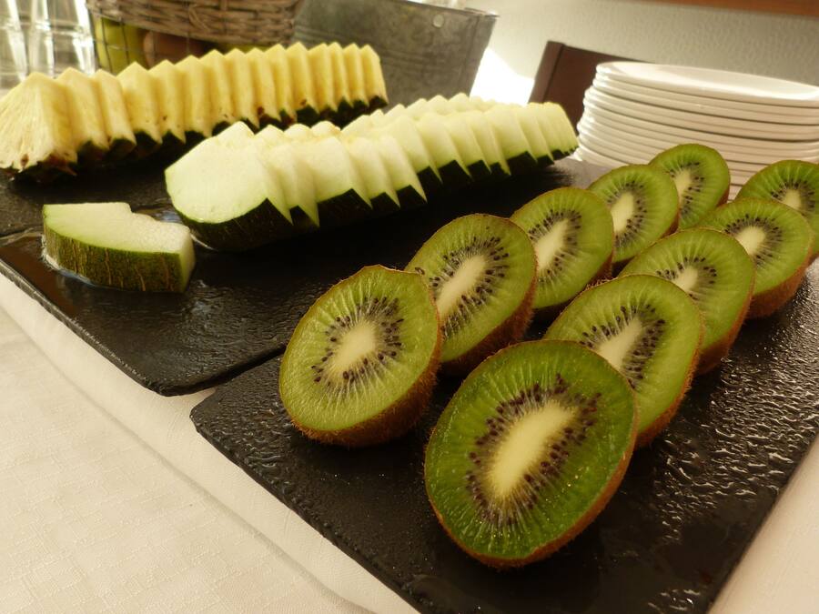 A table with sliced kiwi and cucumber arranged on a black slate.