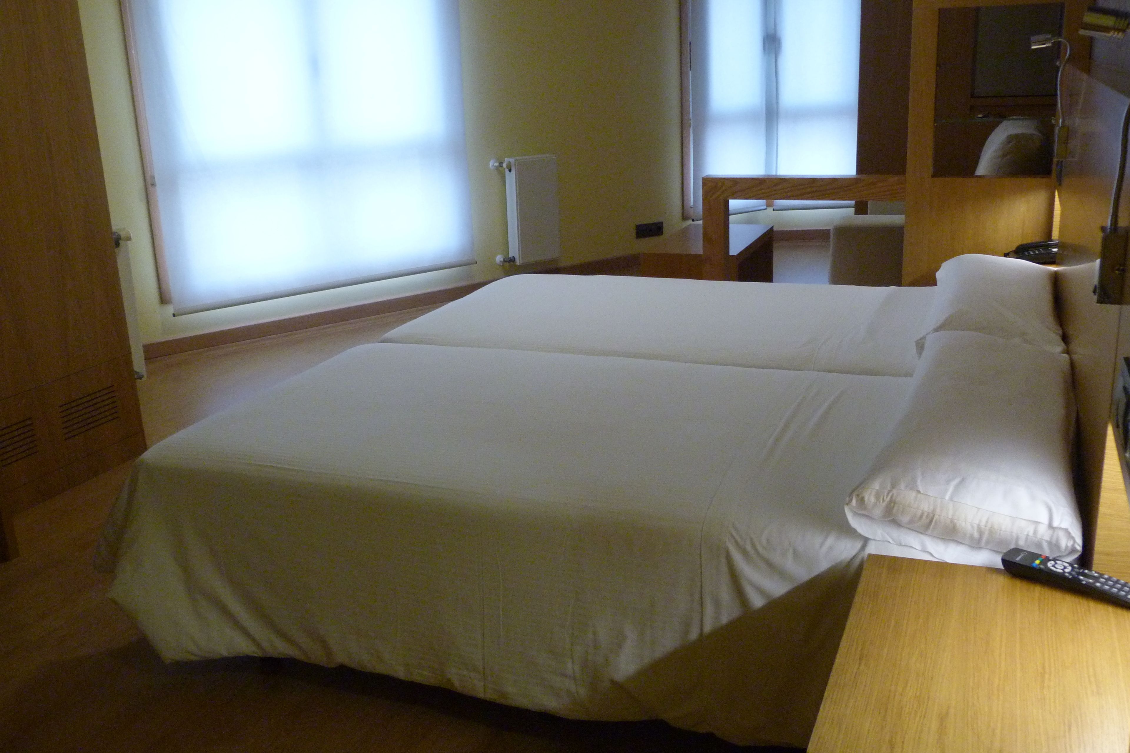 Una habitación de hotel con una cama grande, una mesita de noche de madera y un control remoto sobre la mesita.