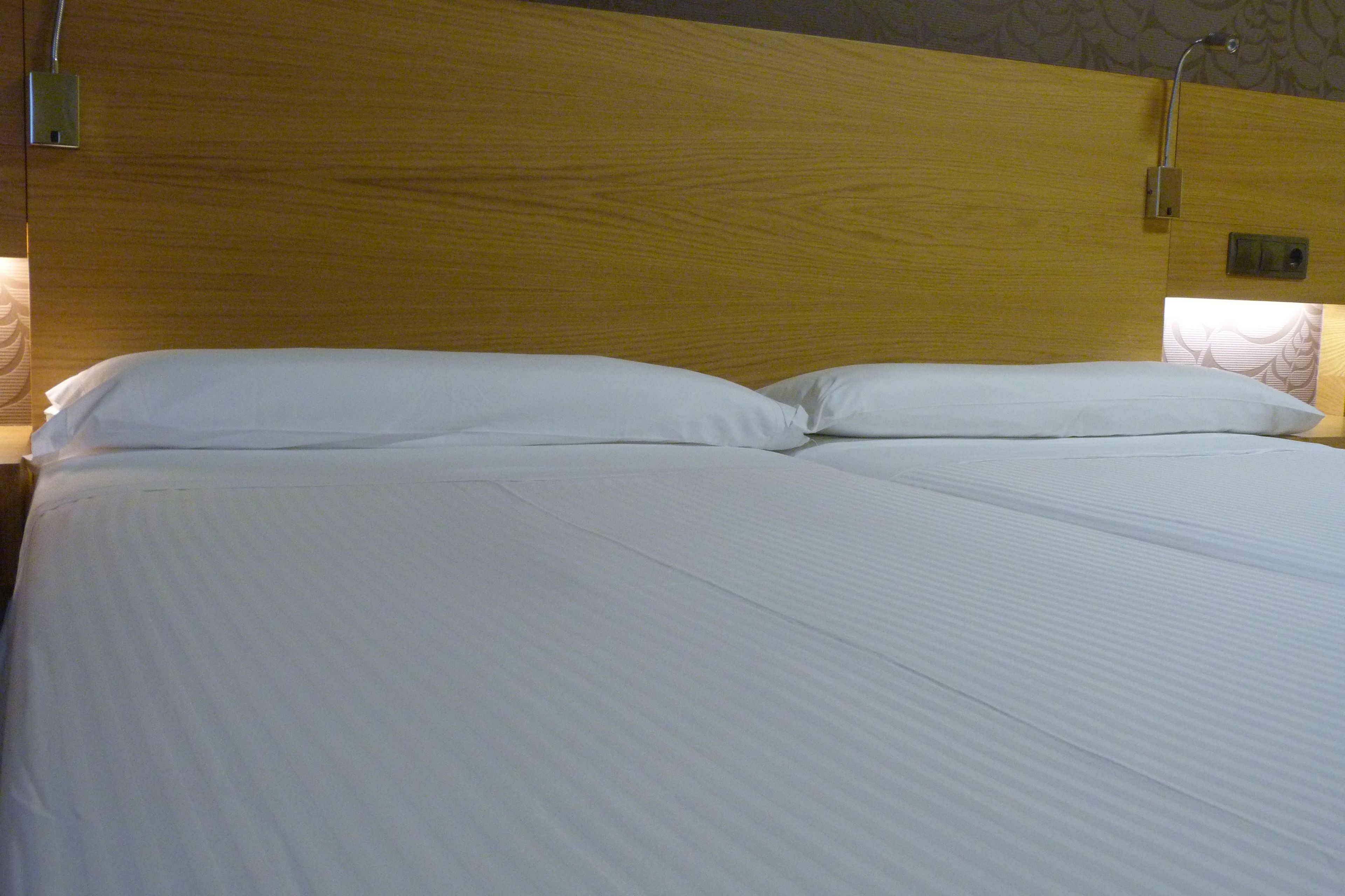 A neatly made bed with white linens and a wooden headboard.
