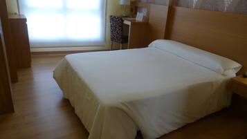 Una cama bien hecha en una habitación de hotel, con cabecera de madera, mesita de noche y lámpara.