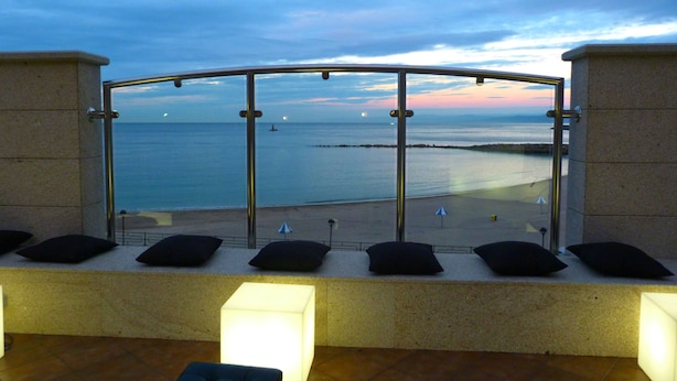 A balcony with a glass railing overlooking a beach at dusk.