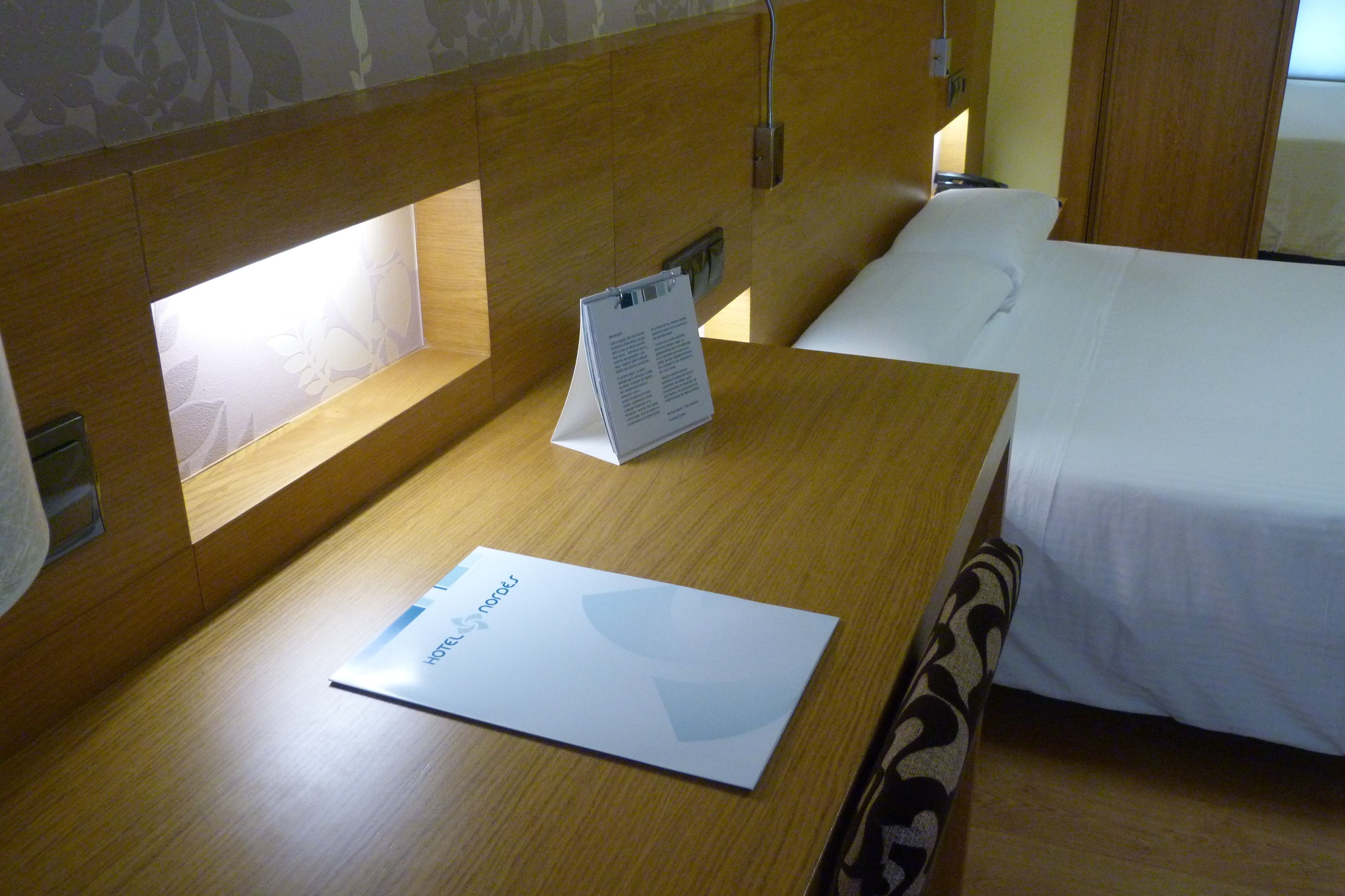 A hotel room with a wooden headboard, a bedside table with a menu, and a bed with white linens.