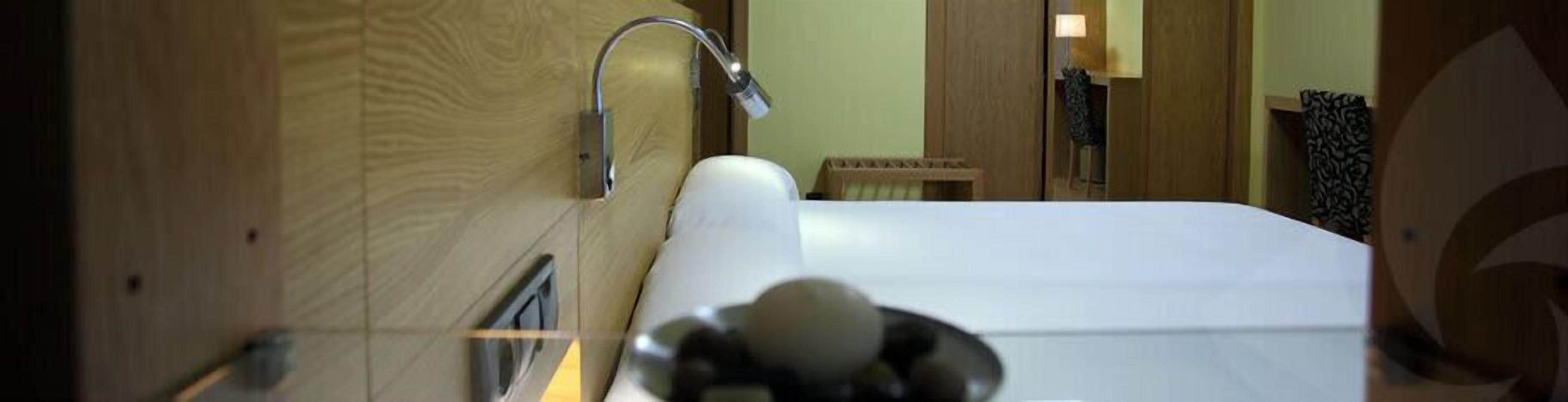 Une chambre d’hôtel avec un grand lit, une tête de lit en bois, une salle de bain avec douche et un petit coin salon.