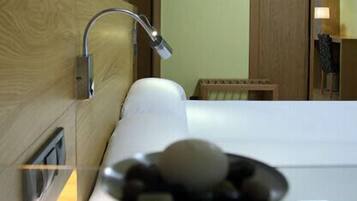 Une chambre d’hôtel avec un grand lit, une tête de lit en bois, une salle de bain avec douche et un petit coin salon.