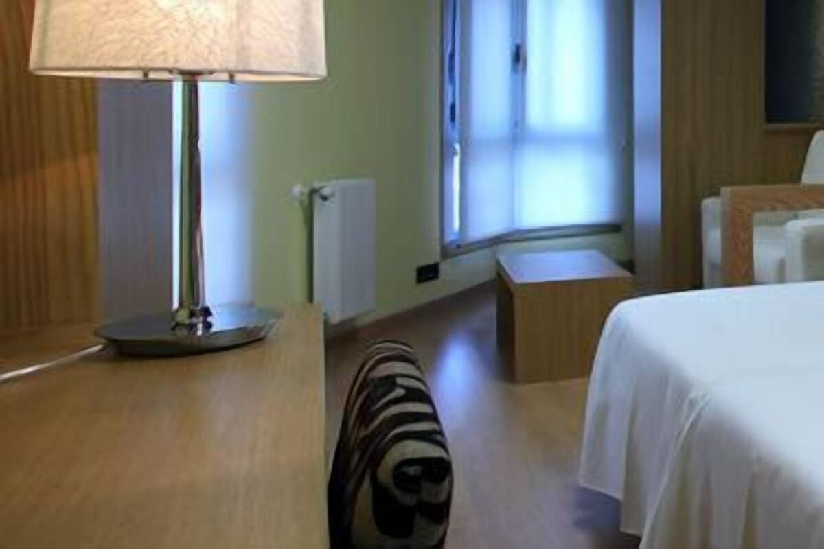 A hotel room with a large bed, bedside tables, a lamp, and a mirror.