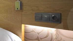 A bed with white linens in a room with wooden headboard and a wall-mounted control panel.