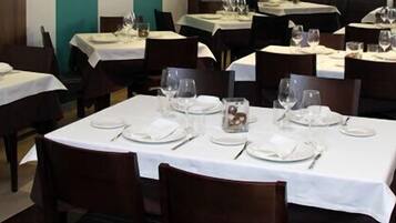 Un restaurante con varias mesas dispuestas, cada una con manteles blancos, platos, cubiertos y vasos.