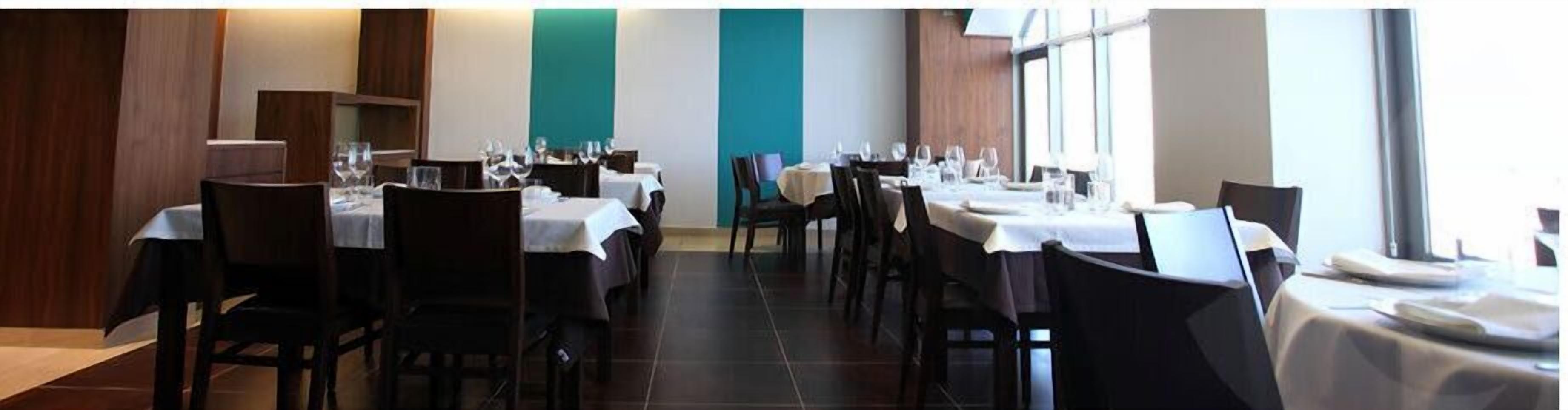A restaurant with multiple tables set for dining, featuring a modern interior design with dark wooden chairs and white tablecloths.
